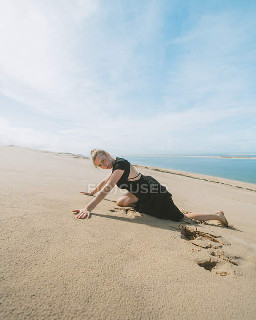 Vista laterale del corpo pieno di ballerina a piedi nudi nella sabbia che tende le braccia mentre guarda la fotocamera nel deserto sabbioso — Foto stock