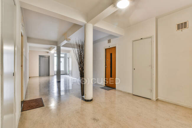 Современный коридор с ковровым покрытием на полу и колоннами с блестящей лампой на потолке между дверями — стоковое фото