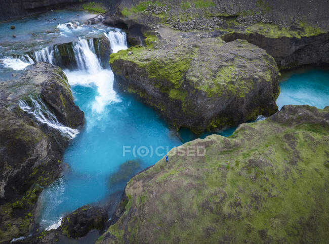 De cima de cascata rápida caindo em lago azul cercado por formações rochosas ásperas cobertas com musgo verde na natureza da Islândia — Fotografia de Stock