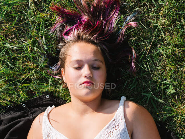 Вид зверху розслабленої надмірної ваги жінки з фарбованим волоссям і закритими очима, відпочиваючи на трав'янистому газоні в сонячний день — стокове фото