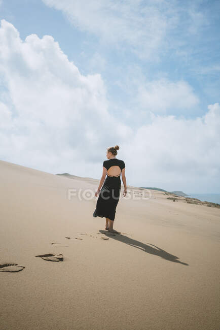 Full body back view of unrecognizable barefoot female in dress strolling on sandy dune in desert — Stock Photo