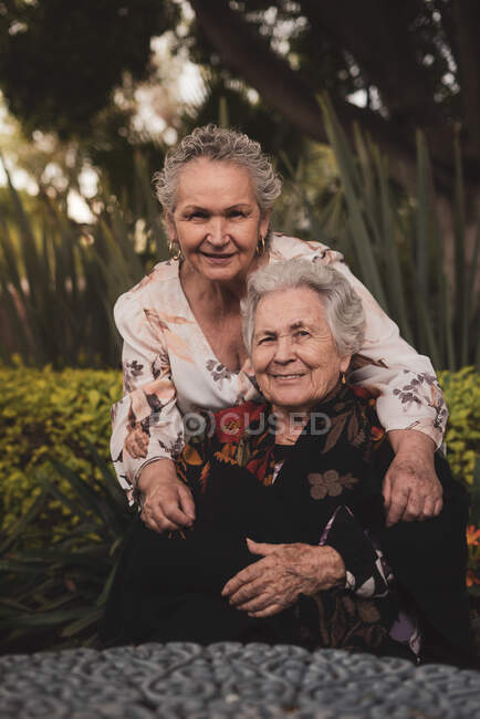 Glücklich gealterte Frau umarmt Schwester auf dem Kopf und lächelt dann in die Kamera, während sie Zeit im Garten zusammen verbringt — Stockfoto