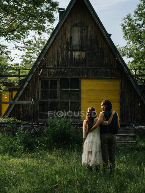 Вид ззаду привабливої пари, що обіймається перед старим дерев'яним будинком — стокове фото