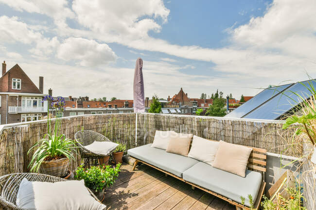 Amplia y acogedora terraza de casa residencial con cómodo sofá y sillas decoradas con plantas en maceta en un día soleado - foto de stock