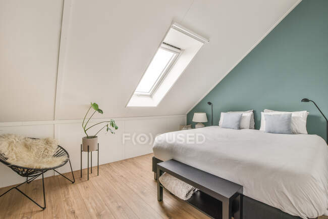 Комфортне ліжко з подушками, розташованими біля вікна в світлій горищній спальні в сучасному будинку — стокове фото