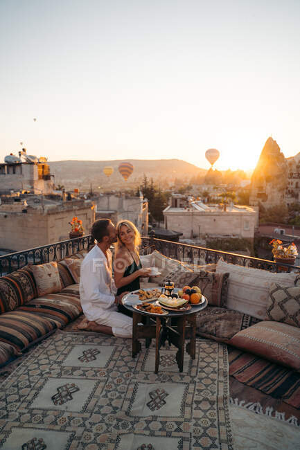 Vista lateral de amar a la esposa abrazadora masculina mientras comen postre y beben té juntos en la terraza - foto de stock