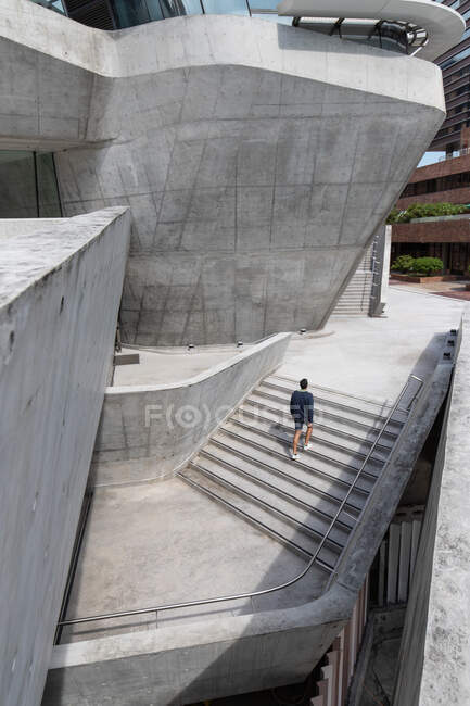 From above back view of unrecognizable guy walking upstairs of contemporary geometric building located in Hong Kong on sunny day — Stock Photo