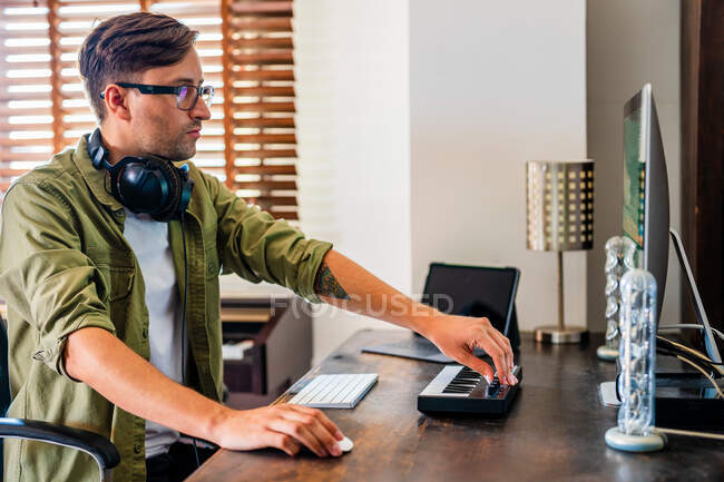 Side view of concentrated guy with headphones on neck sitting at table and using mouse while working on computer — Stock Photo