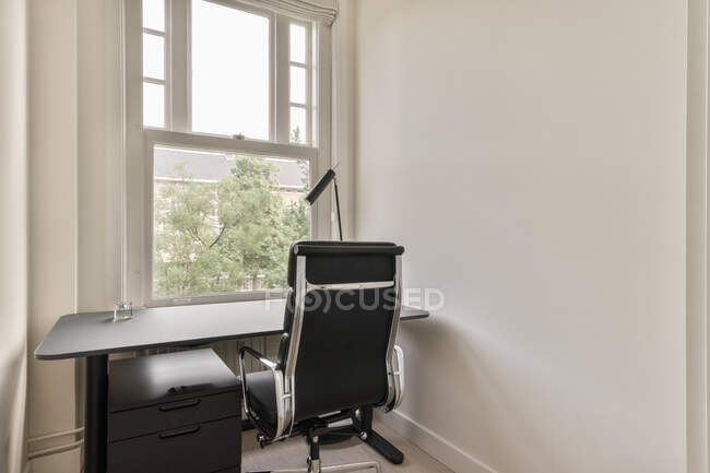 Schwarzer Tisch mit Schrank und bequemem Lederstuhl in Fensternähe im hellen Home Office — Stockfoto