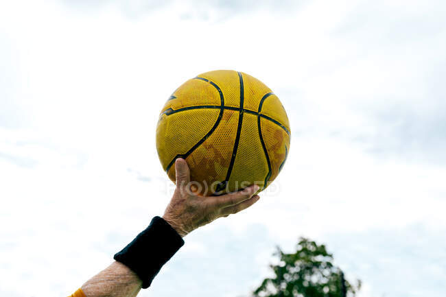 Ernte anonyme reife Person mit gelbem Basketballball in der Hand steht auf öffentlichem Sportplatz beim Spielen auf der Straße — Stockfoto