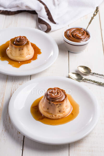 From above of egg custards topped with sweet Dulce de leche served on white plates on table with cutlery in kitchen — Stock Photo
