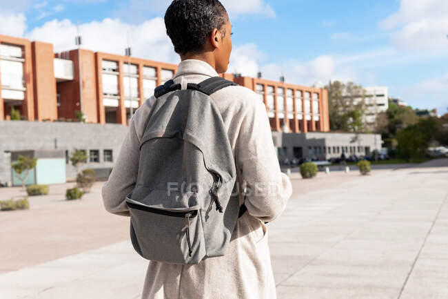 Vista posteriore di studentessa afroamericana anonima con zaino in piedi sulla passerella vicino al moderno edificio universitario sulla strada — Foto stock