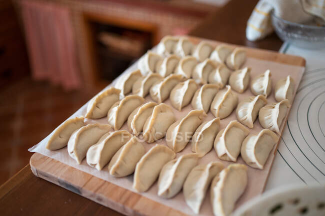 D'en haut des boulettes de jiaozi traditionnelles crues servies sur une planche à découper en bois dans la cuisine — Photo de stock