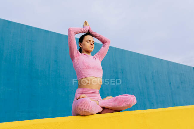 Full body of barefoot female in activewear sitting in lotus pose with raised arms and closed eyes — Stock Photo