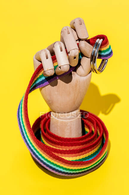Main artificielle avec un long bracelet de couleur arc-en-ciel avec des anneaux de boucle en métal placés sur fond jaune dans un studio moderne créatif léger — Photo de stock