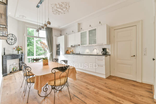 Innenraum der geräumigen Küche mit weißen Möbeln mit eingebauten Geräten und Esstisch im Tageslicht — Stockfoto