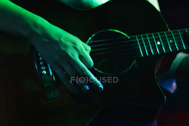Cropped guitarrista feminina irreconhecível tocando guitarra acústica no clube de luz — Fotografia de Stock