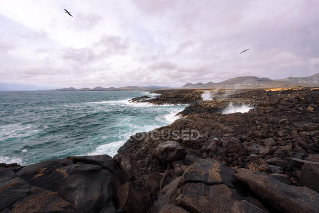 Сценический вид на пенный океан против пляжа Чиклос и вулкана Гинчо в Голфо-Яиса-Лансароте Канарские острова Испания — стоковое фото