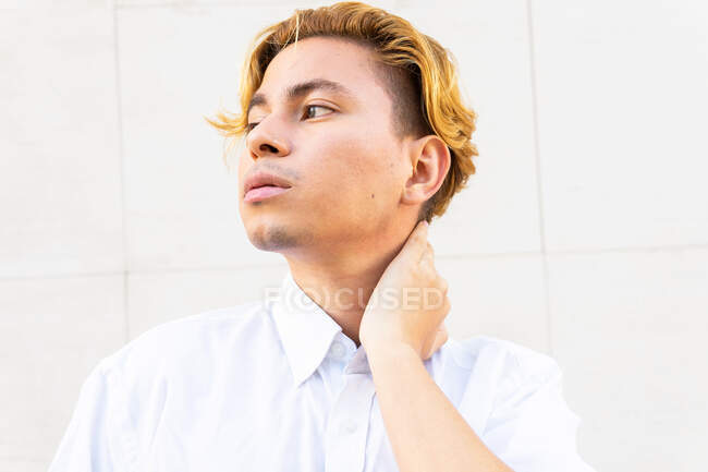 Serious young male looking into distance with thoughtful glance while standing near white wall on street — Stock Photo