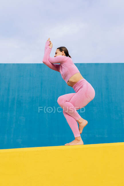 Passgenaue Frau in rosa Sportbekleidung balanciert auf Bein, während sie Yoga-Übungen gegen blaue Wand macht — Stockfoto