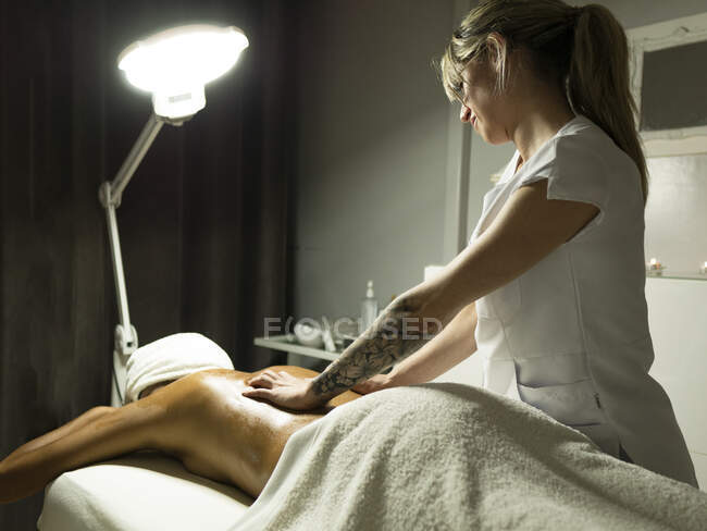 Unrecognizable female masseur massaging back of client in towel on couch in light spa center — Stock Photo
