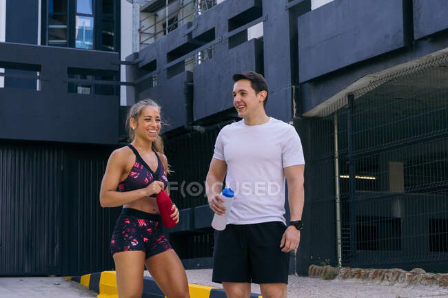 Positive fit sportspeople in activewear standing with bottles of water while recovering after training together — Stock Photo