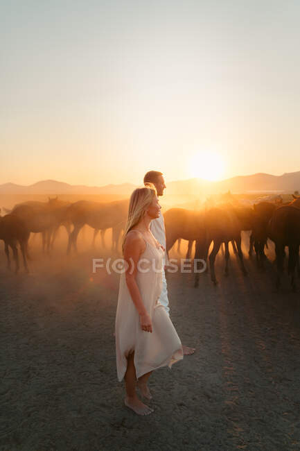 Full body of loving woman and man holding hands and looking away while walking in countryside in sunset — Stock Photo