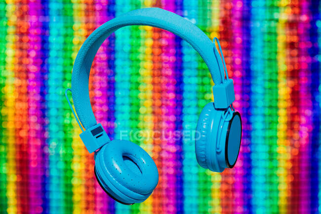 Auriculares inalámbricos azules brillantes contemporáneos para escuchar música colgando contra un fondo de neón colorido - foto de stock