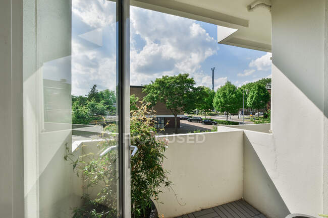 Balcone con recinzione bianca e pianta contro alberi verdi sotto il cielo nuvoloso nella città soleggiata — Foto stock
