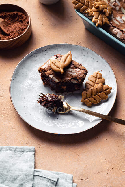 Slice of sweet fresh baked chocolate brownie with cookies served on plate near baking pan on table with cup of coffee — Stock Photo