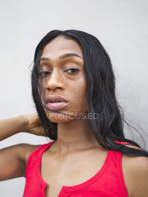 Mujer afroamericana segura con el pelo negro mirando a la cámara mientras está de pie sobre fondo blanco en la calle - foto de stock
