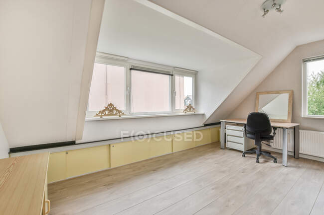 Interno di camera moderno con pannello su scrivania contro poltrona su parquet in soffitta di casa con finestre di giorno — Foto stock