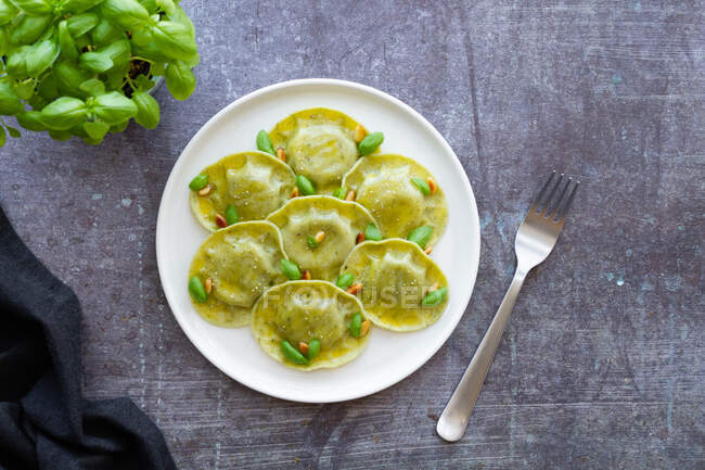 Top view of tasty raviolis with basil decorated with pine nuts served on white round plate on table in light kitchen — Stock Photo