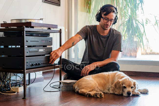 Человек подключение наушников к игроку, сидя на полу с Cocker спаниель щенок в светлой комнате — стоковое фото
