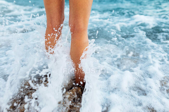 Dall'alto del raccolto irriconoscibile viaggiatore femminile scalzo in piedi sulla riva sabbiosa bagnata lavata da onde schiumose — Foto stock