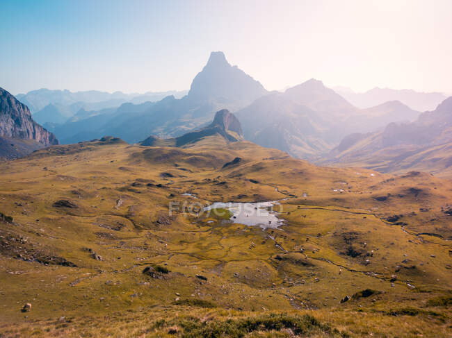 Травянистая местность с небольшим озером, расположенным против грубых крутых гор против безоблачного неба в дикой природе Испании в Пиренеях — стоковое фото