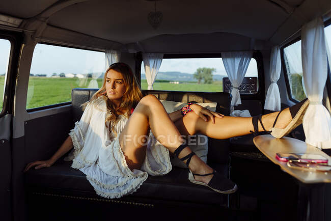 Attractive blonde girl inside a vintage van and lying on the seat on a sunny day looking away — Stock Photo