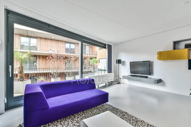 Moderne Wohnzimmereinrichtung mit Sofa und Tisch gegen Fensterwand und Fernseher auf dem Regal im Haus — Stockfoto