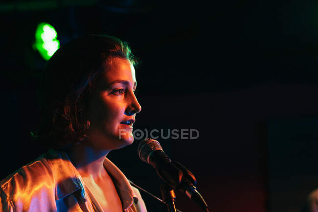 Confident lady with guitar singing in mic while performing song in bright club — Stock Photo