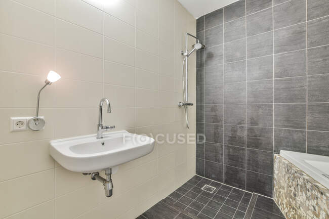 Интерьер современной ванной комнаты с белой и серой плиткой стены и пола раковина светильник душ и ванна — стоковое фото