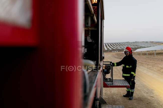 Side view of a firefighter removing a portable light generator from the side of the fire truck — Stock Photo