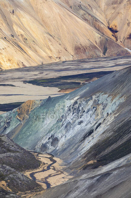 Formazioni rocciose con superficie irregolare ruvida situata a terra vicino a ripida cresta di montagna nella natura dell'Islanda nella giornata di sole — Foto stock
