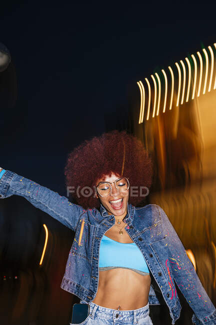 Веселая женщина танцует в солнечных очках, стоя со светом в вечернее время — стоковое фото