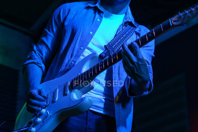Crop anonimo chitarrista maschile suonare la chitarra elettrica nel club con luci blu neon — Foto stock