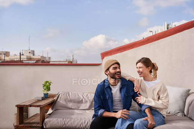Positiver Mann umarmt Freundin, während er auf bequemer Couch sitzt und einander mit zahmem Lächeln ansieht — Stockfoto