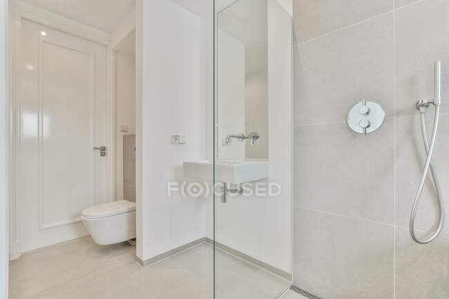 Waschbecken an Wand zwischen Toilette und Glasduschkabine im hellen minimalistischen Badezimmer installiert — Stockfoto