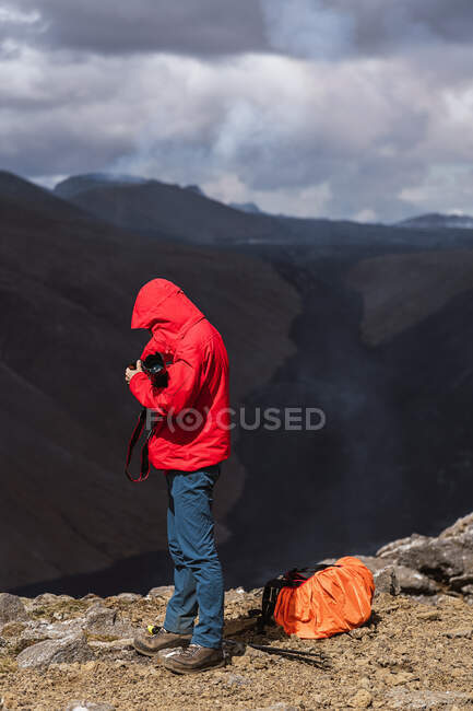 Seitenansicht eines männlichen Fotografen in Oberbekleidung auf einer Felsklippe in der Nähe des aktiven Vulkans Fagradalsfjall mit schwarzer Lava in Island bei Tag — Stockfoto