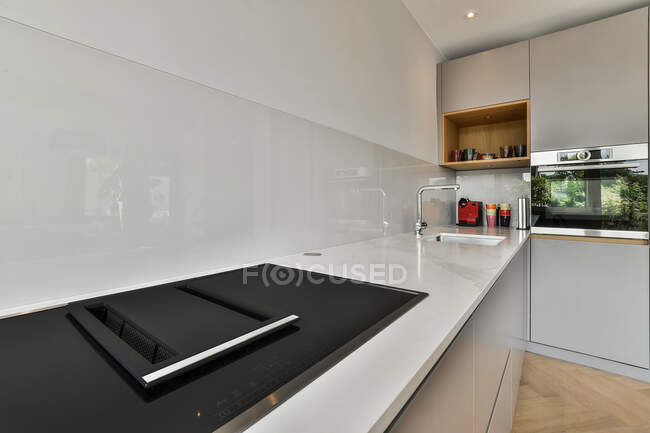 Modern kitchen interior with built in electric stove and oven against sink at home in daytime — Stock Photo
