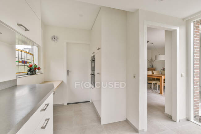 Interior de cozinha moderna com construído em microondas e forno contra mesa em casa com piso em azulejo — Fotografia de Stock