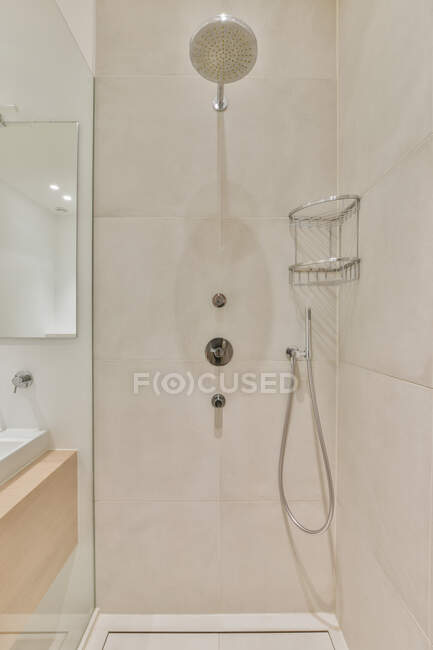 Shower head with hose at wall with tiles and shower caddy near mirror with reflection in modern light washroom in apartment — Stock Photo